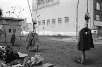 Image of sheet 19900730 photo 1: Am Checkpoint Charlie in Berlin verkaufen Polen alte DDR Uniformen und Flaggen etc. Im Hintergrund steht 'Neue Zeit'. Verkäufer ist uniformiert. Alter Mann hinter den Mützen. 
Former Checkpoint Wallborder to East-Germany GDR. An old Polish Citizen is sitting near old military uniforms from various Eastern Countries. The Pole is selling these uniforms to travellers who visit whatever is left over from the 'Wall'.

Potsdamer-Platz ist besetzt von Obdachlosen in Zelten. Refugees from the Eastern block are sitting in front of their tents on the Potsdamerplatz near the former wall that divided East- and Westgermany. Trabant fährt auf der Ebertstrasse auf ehemaligem Mauerstreifen. Brandenburger Tor Brandenburg Gate ohne Skulptur Quadriga. Frau fotografiert. Schwarzmarkt. Polenmarkt. Volks- Polizei bricht illegale Verkaufsstände ab. Alte kontrolliert ihre Kasse Portemonnaie in Pankov. Deutschland 1990

Checkpoint Charlie (or Checkpoint C) was the name given by the Western Allies to the best-known Berlin Wall crossing point between East Berlin and West Berlin during the Cold War.

The Soviet Union prompted the erection of the Berlin Wall in 1961 to stem the flow of Eastern Bloc emigration westward through what had become a loophole in the Soviet border system, preventing escape over the city sector border from East Berlin to West Berlin. Checkpoint Charlie became a symbol of the Cold War, representing the separation of east and west, and—for some East Germans—a gateway to freedom. Soviet and American tanks briefly faced off at the location during the Berlin Crisis of 1961.