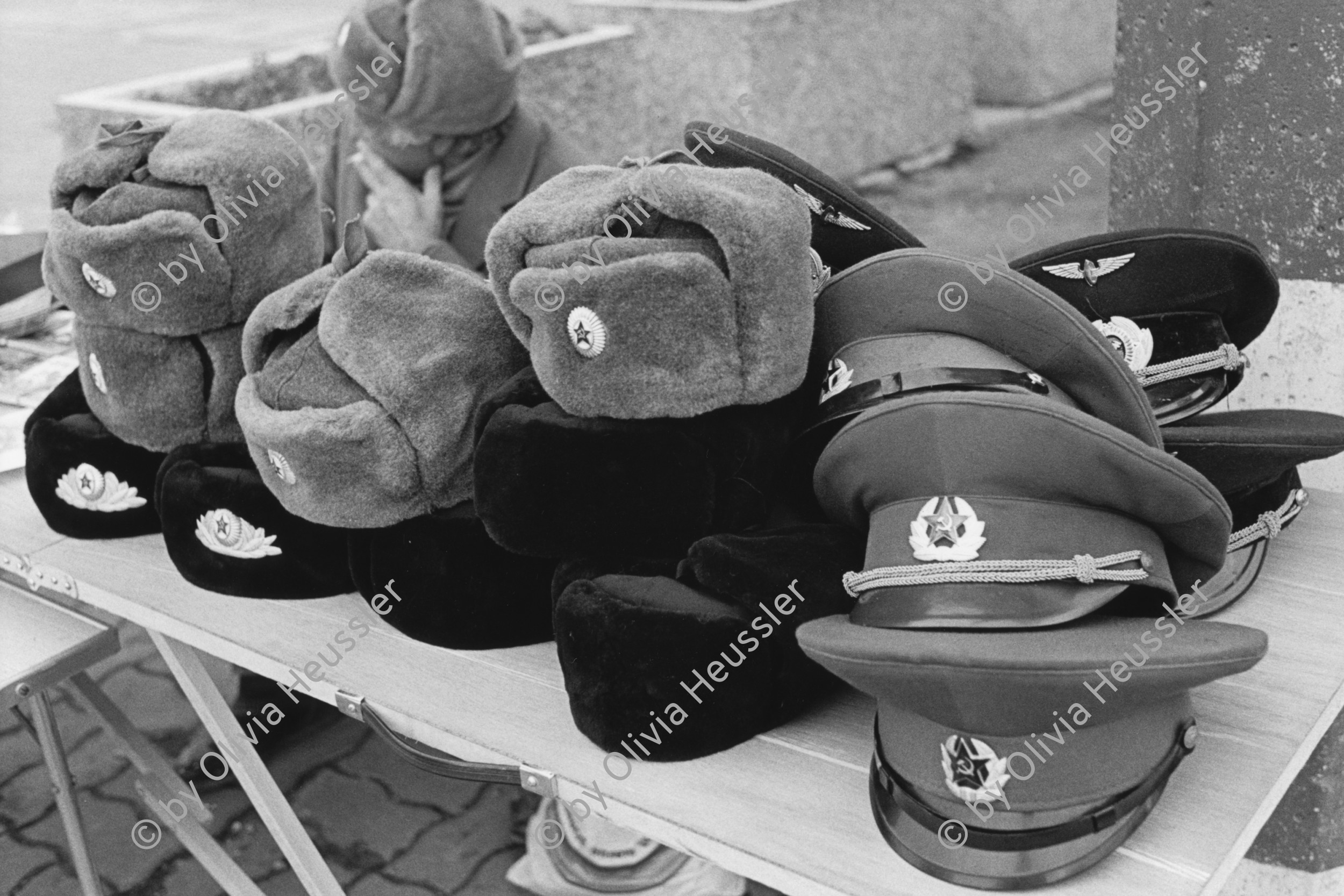 Image of sheet 19900730 photo 15: Am ehemaligen Checkpoint Charlie werden ausgediente Uniformen aus dem Osten feilgeboten. √ hut caps
Former Checkpoint Wallborder to East-Germany GFR. An old Polish Citizen is sitting near old military uniforms from various Eastern Countries. The Pole is selling these uniforms to travellers who visit whatever is left over from the 'Wall'. Berlin 1990