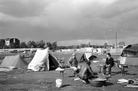 Image of sheet 19900730 photo 19: © 1990, Olivia Heussler / www.clic.li
Potsdamer-Platz ist besetzt von Obdachlosen in Zelten. Refugees from the Eastern block are sitting in front of their tents on the Potsdamerplatz near the former wall that divided East- and Westgermany. Ebertstrasse auf ehemaligem Mauerstreifen. Deutschland 1990 √ Berlin

Potsdamer Platz (German: [potsdamaː plats] ( listen), literally Potsdam Square) is an important public square and traffic intersection in the centre of Berlin, Germany, lying about one kilometre south of the Brandenburg Gate and the Reichstag (German Parliament Building), and close to the southeast corner of the Tiergarten park. It is named after the city of Potsdam, some 25 km to the south west, and marks the point where the old road from Potsdam passed through the city wall of Berlin at the Potsdam Gate. After developing within the space of little over a century from an intersection of rural thoroughfares into the most bustling traffic intersection in Europe it was totally laid waste during World War II and then left desolate during the Cold War era when the Berlin Wall bisected its former location. Since German reunification, Potsdamer Platz has been the site of major redevelopment projects.