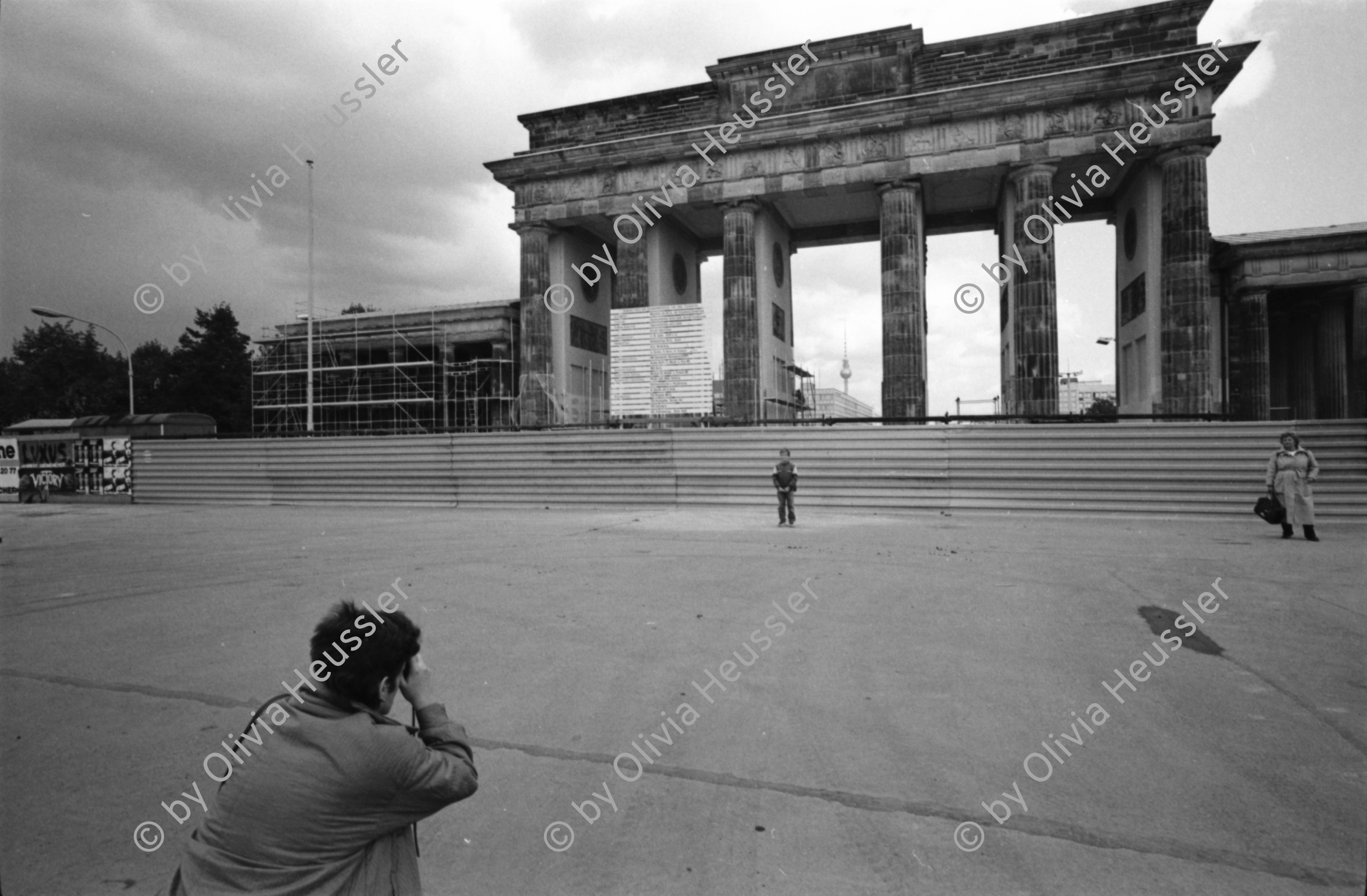 Image of sheet 19900730 photo 24: Brandenburg Gate ohne Skulptur Quadriga. Frau fotografiert. Schwarzmarkt. Polenmarkt. Volks- Polizei bricht illegale Verkaufsstände ab.