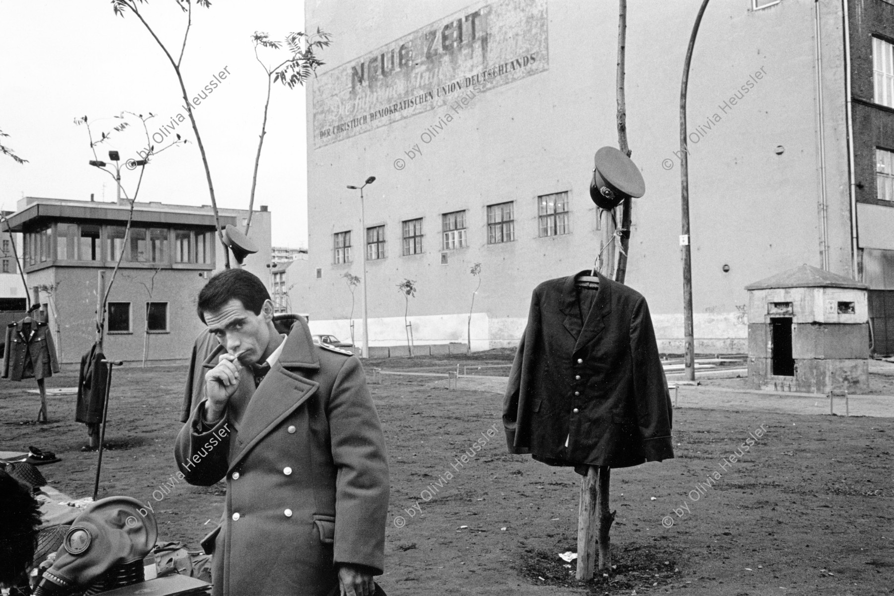 Image of sheet 19900730 photo 3: © 1990, OLIVIA HEUSSLER / www.clic.li
Am Checkpoint Charlie in Berlin verkaufen Polen alte DDR Uniformen und Flaggen etc. Im Hintergrund steht 'Neue Zeit'. Verkäufer ist uniformiert.  
Former Checkpoint Wallborder to East-Germany GDR. An Polish Citizen  near old military uniforms from various Eastern Countries. The Pole is selling these uniforms to travellers who visit whatever is left over from the 'Wall'.

Deutschland 1990 √

Checkpoint Charlie (or Checkpoint C) was the name given by the Western Allies to the best-known Berlin Wall crossing point between East Berlin and West Berlin during the Cold War.

The Soviet Union prompted the erection of the Berlin Wall in 1961 to stem the flow of Eastern Bloc emigration westward through what had become a loophole in the Soviet border system, preventing escape over the city sector border from East Berlin to West Berlin. Checkpoint Charlie became a symbol of the Cold War, representing the separation of east and west, and—for some East Germans—a gateway to freedom. Soviet and American tanks briefly faced off at the location during the Berlin Crisis of 1961.