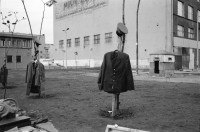 Image of sheet 19900730 photo 4: Am Checkpoint Charlie in Berlin verkaufen Polen alte DDR Uniformen und Flaggen etc. Im Hintergrund steht 'Neue Zeit'. Verkäufer ist uniformiert. Alter Mann hinter den Mützen. 
Former Checkpoint Wallborder to East-Germany GDR. An old Polish Citizen is sitting near old military uniforms from various Eastern Countries. The Pole is selling these uniforms to travellers who visit whatever is left over from the 'Wall'.

Potsdamer-Platz ist besetzt von Obdachlosen in Zelten. Refugees from the Eastern block are sitting in front of their tents on the Potsdamerplatz near the former wall that divided East- and Westgermany. Trabant fährt auf der Ebertstrasse auf ehemaligem Mauerstreifen. Brandenburger Tor Brandenburg Gate ohne Skulptur Quadriga. Frau fotografiert. Schwarzmarkt. Polenmarkt. Volks- Polizei bricht illegale Verkaufsstände ab. Alte kontrolliert ihre Kasse Portemonnaie in Pankov. Deutschland 1990

Checkpoint Charlie (or Checkpoint C) was the name given by the Western Allies to the best-known Berlin Wall crossing point between East Berlin and West Berlin during the Cold War.

The Soviet Union prompted the erection of the Berlin Wall in 1961 to stem the flow of Eastern Bloc emigration westward through what had become a loophole in the Soviet border system, preventing escape over the city sector border from East Berlin to West Berlin. Checkpoint Charlie became a symbol of the Cold War, representing the separation of east and west, and—for some East Germans—a gateway to freedom. Soviet and American tanks briefly faced off at the location during the Berlin Crisis of 1961.