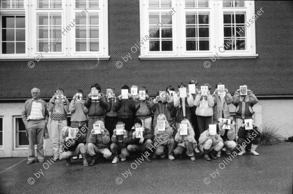 Image of sheet 19900930 photo 8: frtsg. 900920 Schulklasse spielt vor Schulhaus auf Pausenhof. Gruppenbild jedes Kind trägt die Flagge Fahne seines Herkunftsland. Eine Türkin etc. Primarlehrer Primarschule Lehrer Thöny vor seinen Photographien. 5 und 6. Klasse. Buben mit typischem Appenzeller Ohrschmuck. Urnäsch im Kanton Appenzell Ausserrhoden