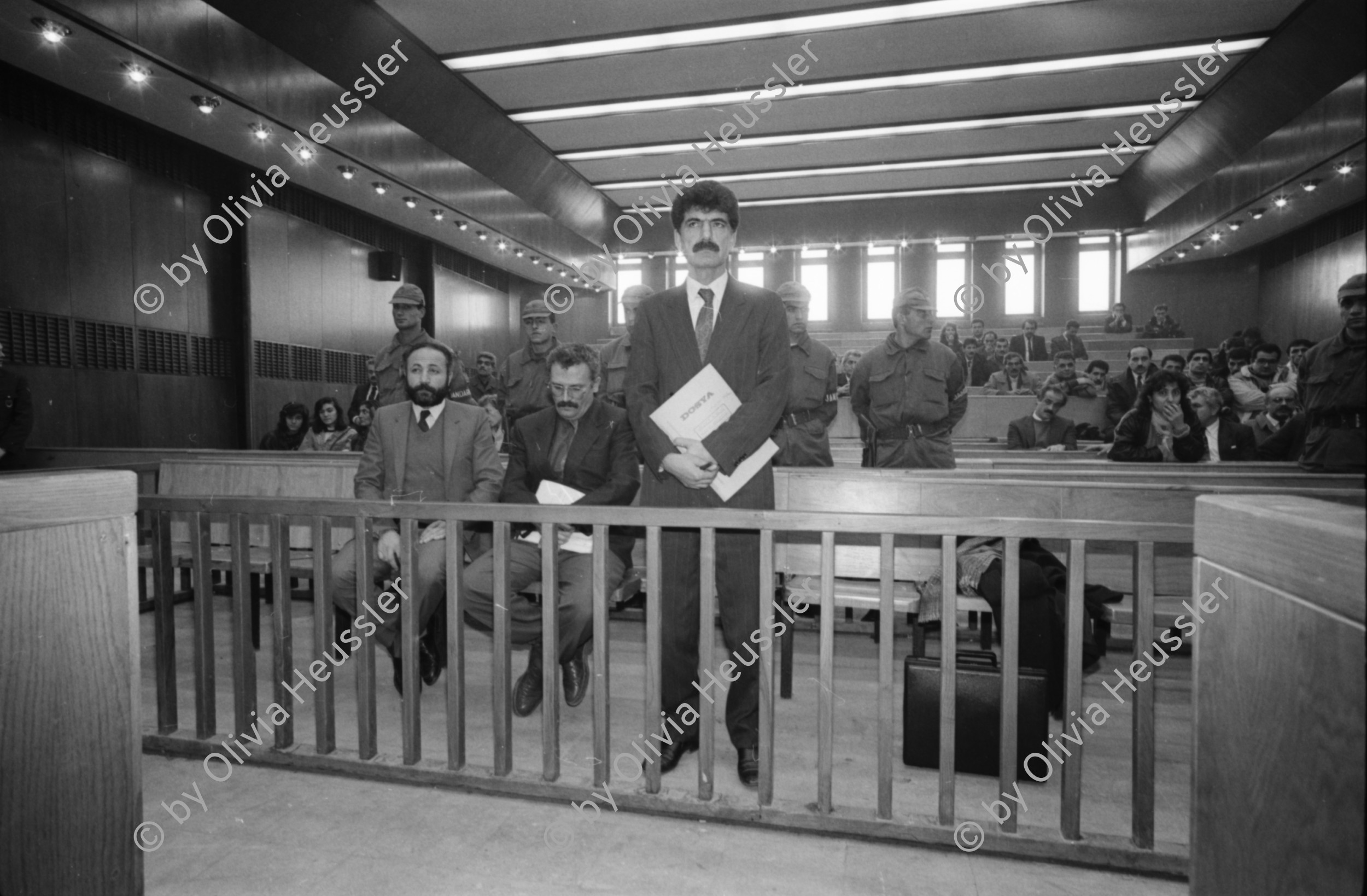 Image of sheet 19901090 photo 36: Staatssicherheitsgericht. Prozess gegen die kurdischen Anwälte: Vedat Aydin, Zeki Okçuoğlu und Mustafa Oezer.  Die angeklagten kurdischen Anwälte v.l.n.r. Vedat Aydin, Ahmet Zeki Okçuoğlu, und Mustafa Oezer während einem Prozess im Ankaraer Staatsgericht stehen vor dem Staatsrichter in der Anklagebank. Kurds Kurdish Turkey Ankara Dec. 1990 

Vor dem Eingang des Staatssicherheitsgericht.

Lissy Schmidt (am 3.4.94 im Irak umgebracht) a German freelance journalist who worked with Agence France-Presse and the German newspapers Frankfurter Rundschau and Der Tagesspiegel, and a friend were shot and killed when gunmen opened fire on their car outside the city of Sulaymaniyah in the Kurdish-controlled area of northern Iraq.-
Dort fotografierte ich den Staatsrichter, was er nicht mochte und protestierte. Eine junge Verteidigerin sprach für mich ein Plädoyer.
Nr. 36 Mustafa Oezer steht in der Anklagebank. 
Türkei Kurdische Ostanatolien √
