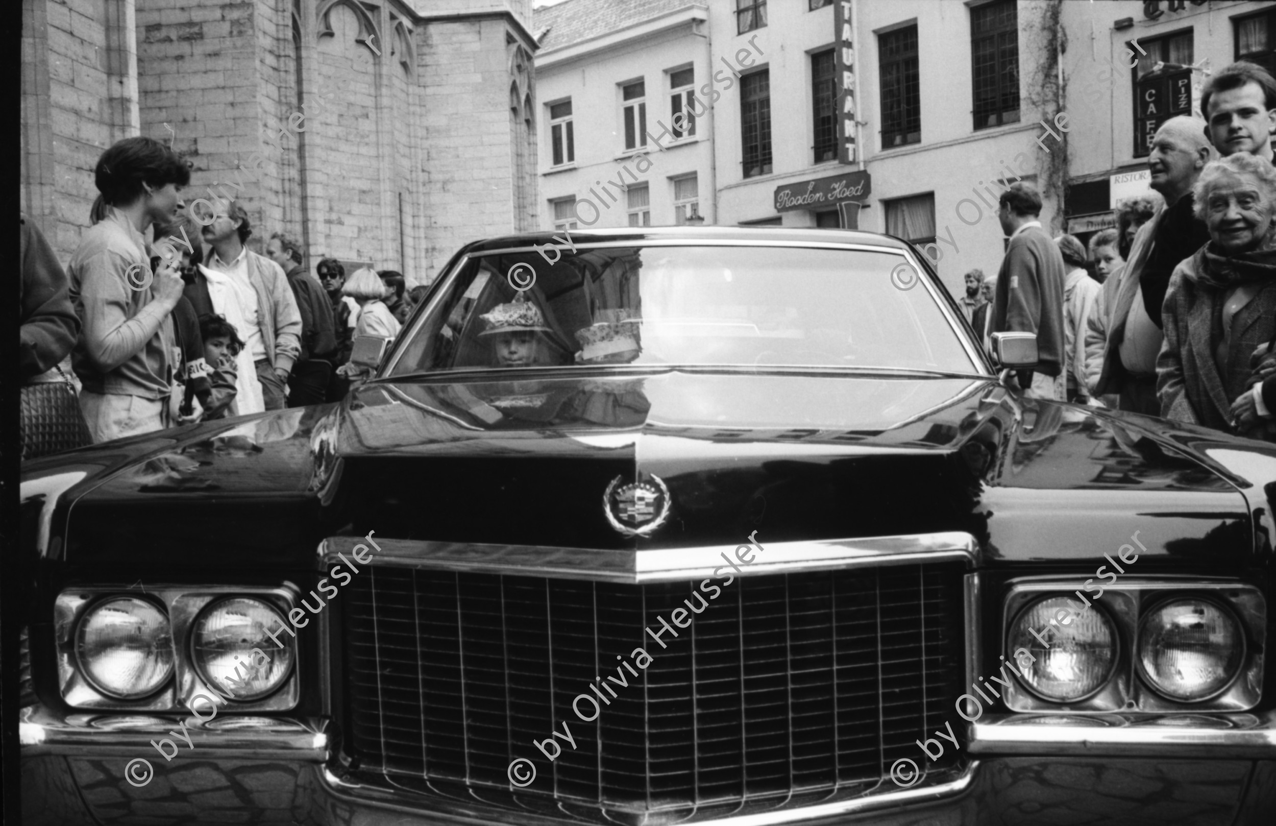 Image of sheet 19910220 photo 12: Strassenszenen in Antwerpen. Nachdenkliche Personen im Café. Frauen. Stühle aufgereiht. Hochzeitsfest in einer Kathedrale. Die Paare werden in grossen eleganten Fahrzeugen Autos abgeholt. Fensterputzerin. Strassenmusikant. Portrait Urs Tremp. Katzen liegen in einem Schaufenster. Drugstore Drogen 5.- Diener mit Mütze eines Chauffeurs einer Karosse. Zwei Mädchen sitzen in der Limousine. Uniform bilder. Belgien 1991