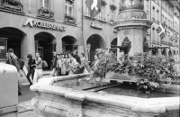 Image of sheet 19910550 photo 2: alter Brunnen Altstadt Bern. Leute sitzen in Biergarten. Italienische Pizzeria. Frau wird von Hund gezogen. Junger Punk sitzt auf Spielzeug. Mädchen vor Wandmalerei Graffiti Olivia. Kleiner portabler TV. Im Zug sitzt Franziska Oliver und Emanuel Tschumi. Olivia. Heussler 1991 Schweiz Bern