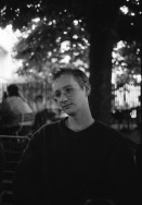 Image of sheet 19910550 photo 29: alter Brunnen Altstadt Bern. Leute sitzen in Biergarten. Italienische Pizzeria. Frau wird von Hund gezogen. Junger Punk sitzt auf Spielzeug. Mädchen vor Wandmalerei Graffiti Olivia. Kleiner portabler TV. Im Zug sitzt Franziska Oliver und Emanuel Tschumi. Olivia. Heussler 1991 Schweiz Bern