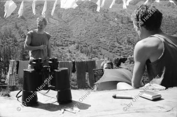 Image of sheet 19910600 photo 35: frtsg. 910610 Jürg Bernhard beim Käsen. Alp Grava Surselva Graubünden. Wäsche im Eimer vor der Hütte. Negro der Hirtenhund Jürg Bernhard nimmt ein kühles Bad im Brunnen. Feldstecher Spiegel steht auf dem Tisch. Miklos Magosch  (31.10.1946 - 25.5.2012) liegt unter Sonnenschirm vor der Hütte. 1991 swiss alps schweiz Switzerland milk cheese production