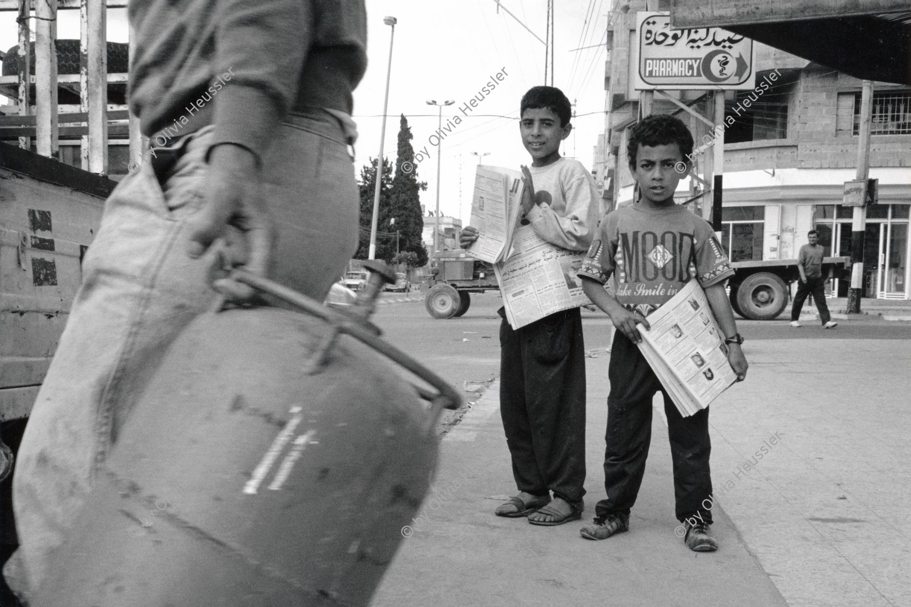 Image of sheet 19920300 photo 24: An einer Kreuzung in Gaza verkaufen zwei Buben die Tages-Zeitung. Tageszeitung Zeitungen Medien Print Mann trägt eine Butan Gas Flasche Kinder Gasflaschen Verkauf

Two Palestinian children selling newspapers in Gaza.
Palästina 04.92  Gazastreifen, Palästina 04.92 Gaza strip Palestine 1992 √

Aus: Out of Jerusalem / Jenseits von Jerusalem
© 1992, OLIVIA HEUSSLER / www.clic.li

RC Print retourned by Libération, Paris 2015