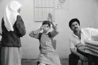 Image of sheet 19920310 photo 35: Die 'Union of Palestinian Medical Relief Committees' organisieren jährlich Gesundheitstage für alle Dorfbewohner Innen. Hier ein präventiver Augentest. in einer Profisorischen Klinik in einer Schule. Westbank occupied teritory 1992 √ Palestine girl uniform school man nurth hairscarf closes eye
The Union of Palestinian Medical Relief Commitees (UPRMC) organizes once a year a health day for all the village inhabitans. Shown here, an eye examination for a schoolgirl student 

Aus: Jenseits von Jerusalem / Out of Jerusalem cover page 57
Exhibition: Out of Jerusalem, Centre Culturel Francais, Jerusalem, Galerie les trois Folles, Zürich