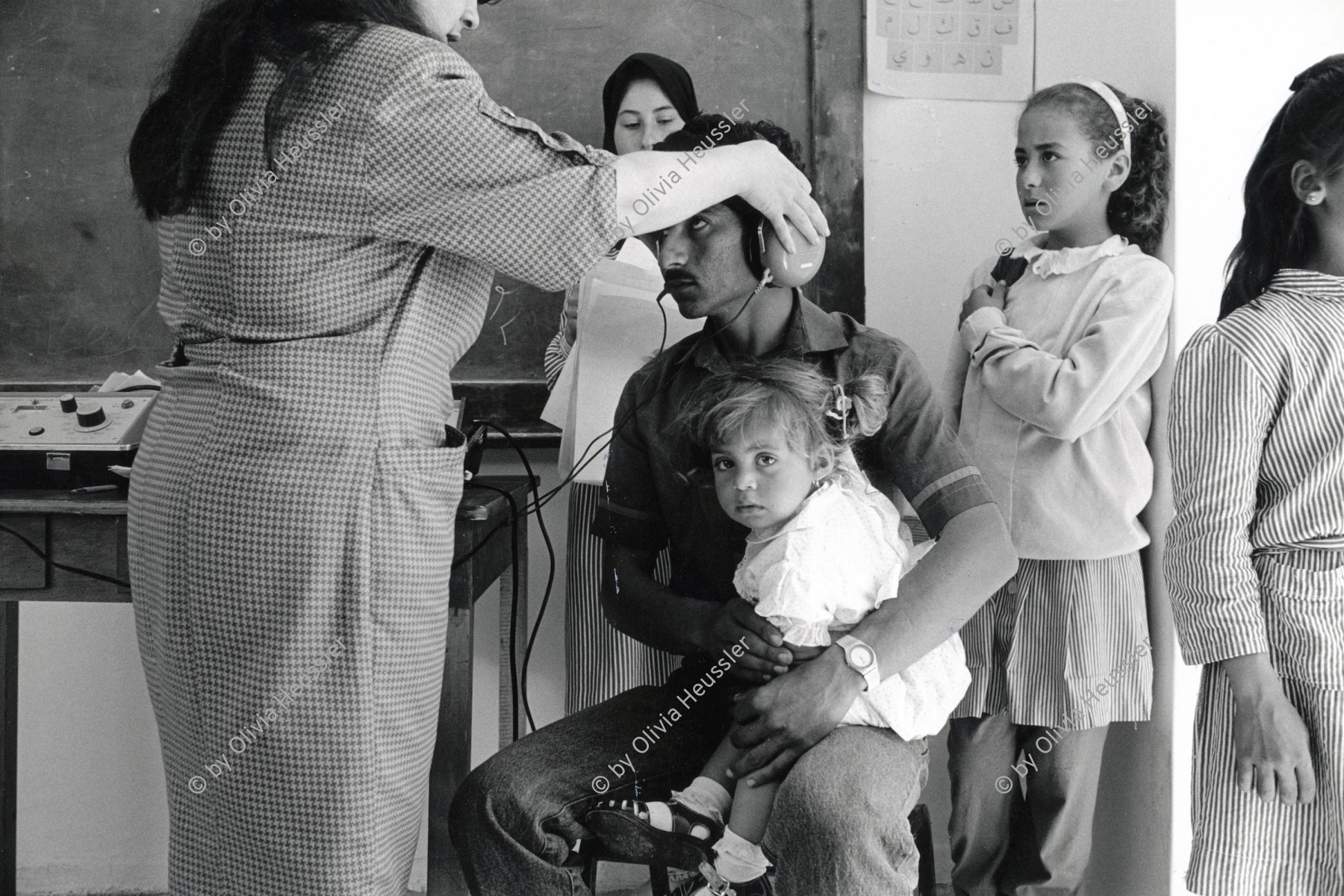 Image of sheet 19920310 photo 37: © 1992, Olivia Heussler / www.clic.li
Die 'Union of Palestinian Medical Relief Committees' organisieren jährlich Gesundheitstage für alle DorfbewohnerInnen. Hier ein präventiver Ohrentest. Jiftlik, Jordantal, Westbank, Palästina. 1992 √

he Union of Palestinian Medical Relief Commitees (UPRMC) organizes once a year a health day for all the village inhabitans. Shown here, an ear examination. Jiftlik, Jordan Valley. Palästina. ear test child man father nurth school girl uniform
al-Jiftlik (Arabic: الجفتلك‎) is a Palestinian town in the West Bank's Jordan Rift Valley several kilometers from the Jordanian border. According to the PCBS statistics for 2006, it was home to 4,401 and set on an area of 81,283 metric dunum.

© 1992, by OLIVIA HEUSSLER / www.clic.li