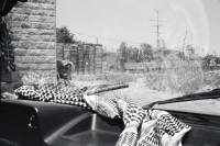Image of sheet 19920430 photo 14: Das palästinensische Kopftuch im Fahrzeug mit gelben, israelischen Schildern, soll vor Steinwürfen schützen.
Westbank occupied territory Palestine 1992 √

Aus: Out of Jerusalem / Jenseits von Jerusalem page 78 , 79 
In a small town on the West Bank, an Israeli barricade is erected to hinder the Intifada. The palestinian headgear (kuffiah) on the car dashboard gives a sense of security to people driving in the occupied Territories with yellow plates