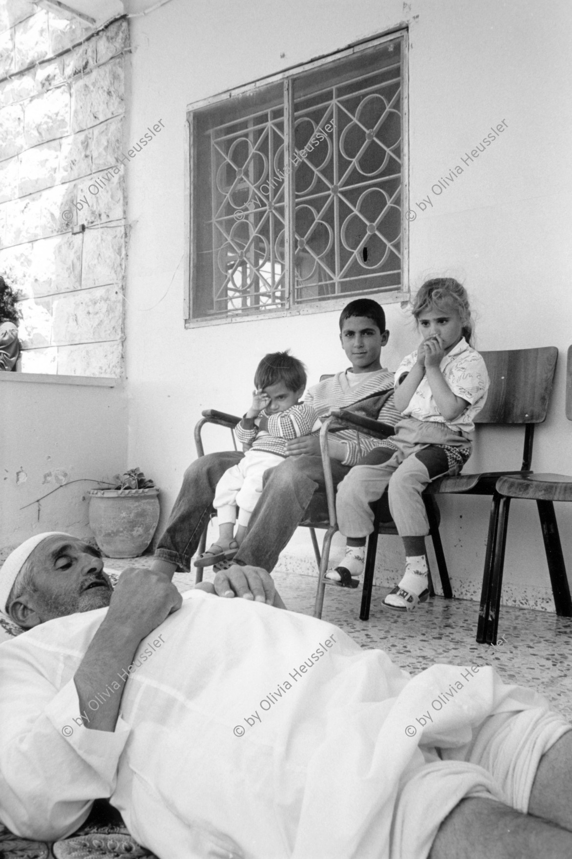 Image of sheet 19920430 photo 7: Ein gehbehinderter Mann wartet zu Hause auf die Hauskrankenpflegerin. Beit Suriq, Westbank. Palästina. 05.92 1992 √ im Hintergrund sitzen seine Enkelkinder 

Physically handicapped patient waiting for a nurse in his house. kids boy girl children old man nurse medical health

handicapped old man is waiting for Etimad, a young Palestinian physical therapist. occupied territory Palestine 1992

Beit Surik (Arabic: بيت سوريك‎) is a Palestinian village in the Jerusalem Governorate, located 12 kilometers Northwest of Jerusalem in the northern West Bank. According to the Palestinian Central Bureau of Statistics, the town had a population of 3,818 in 2006.