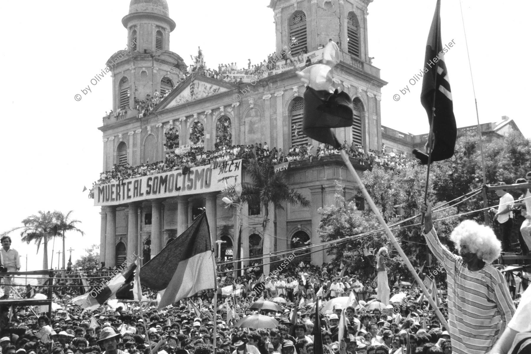 Image of sheet 19930380 photo 34: Menschenmassen Protest Demonstration Jubeln Feier am 19.7.93 auf der Plaza de la Revolucion, vor der Cathedrale Kathedrale:  Managua  ( 14. Jahrestag der sandinistischen Revolution ) FSLN Nicaragua  1993 √  19. Juli 1993
'Muerte al Somocismo' Steht auf dem Banner. Sandinistische flaggen und Fahnen. Clown mit Perrücke 

Durante las celebraciones del 14° aniversario
de la Revolución sandinista. Plaza de la Revolución, Managua, 19 de julio de 1993
Celebrating the 14th anniversary
of the Sandinista revolution.
Plaza of the Revolution, Managua, 1993

Die Kathedrale Santiago de Managua ist die Ruine der alten Kathedrale von Managua. Sie befindet sich an der Plaza de la Revolution, vormals Plaza de la República. Sie wurde als kaschierter Stahlskelettbau im neoklassischen Stil errichtet. Die Fassadenaufteilung ist ähnlich der von St-Sulpice de Paris.