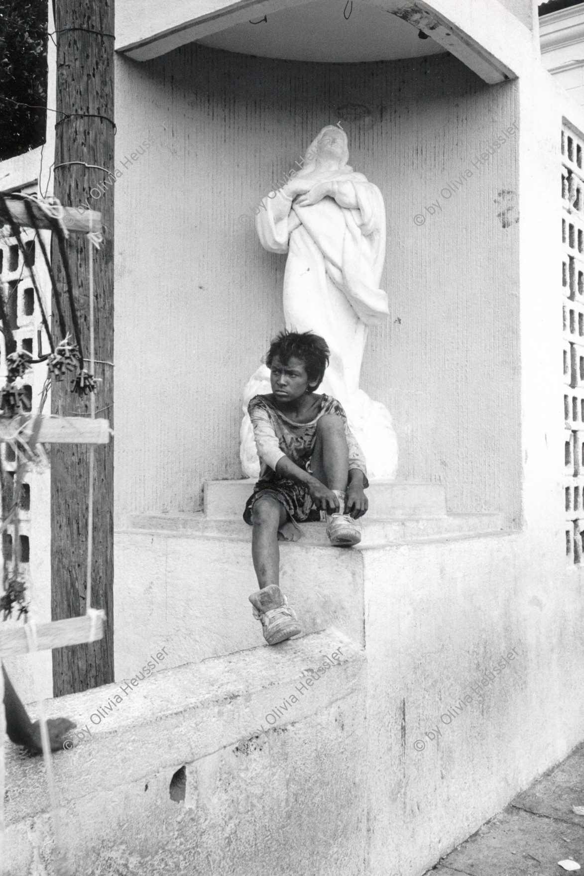 Image of sheet 19930510 photo 17: © 1993, Olivia Heussler / www.clic.li
Ein Strassenjunge sitzt unter einer Statue der Jungfrau Maria. Santo Domingo Managua Nicaragua 07.93 √

en la iglesia «Las Sierritas» en la fiesta patronal de Santo Domingo de Guzmán. Santo Domingo, Dpto. de Managua, 1 de agosto de 1993

in Las Sierritas church at the Patron Saint’s Day festivities for Santo Domingo de Guzmán. Santo Domingo, Dep. Managua, August 1, 1993