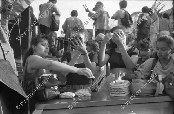 Image of sheet 19930521 photo 3: frtsg. 930520 Fiesta Santo Domingo. Frauen Tänzerinnen schminken sich. Junge Nicaraguaner sind von den Vereinigten Staaten zurückgekehrt. Heimkehrer aus den USA. Coca Cola Stand. Kids. Frau raffelt Guachada. Koch Banane.  Kirche von Santo Domingo mit Sateliten Pfanne am Kirchturm. Tänzerinnen. Apotheke Condega mit gemischten Waren Heilpflanzen sowie schulmedizinische Produkte. Nicaragua 1993 natural health medicine plants pharmacie