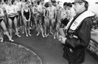 Image of sheet 19940340 photo 1: Polizeiaspirantinnen Polizei und Verkehrspolizisten beamte und Beamtinnen in Badehosen vor der Seeüberquerung Zürichsee Badi Wollishofen. 1600m nach Tiefenbrunnen. Nr. 0 -3 Herr Zurfluh Chef der Ausbildung. Ziel. Nr. 25 Fredi Bachmann Gewinner 32 Minuten. Schwimmer im See Motorboote Polizei. Frau streicht Schwimmer auf Liste mit Fotos. Zürich 1994