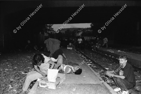 Image of sheet 19940360 photo 22: Mit Turicum (Presse Polizei Hr. Cortesi) Urania, unterwegs mit Polizei wachtmeister Bruno Burri, Nr. 23 und 29 etc. und am Letten. Burri kontrolliert Palästinenser und hilft Schwarzer Frau Drogenszene Leute unter Brücke mit Kreuz im Hintergrund. Schmutz am Boden Junkies fixen. im Dreck. Mann schleppt Mann mit Kartonschachteln weg. Zürich 1994 Junk Fixer