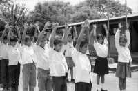 Image of sheet 19950140 photo 17: In der Dorfschule Maurice Demierrre in der Cooperative Santiago Arauz in  Lagartillo bei Achuapa. Die Lehrerin der 2./ 3. und 4. Klasse heisst Janet Alvaro Taruno, 31. Die Lehrerin mit langen Haaren heisst: Digna Reyes, 25. 1. und 4. Klasse. Turnen im Freien. Kinder in Uniformen und an Wandtafel. 1995 Nicaragua