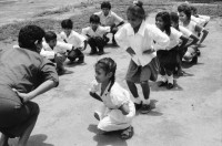 Image of sheet 19950140 photo 30: In der Dorfschule Maurice Demierrre in der Cooperative Santiago Arauz in  Lagartillo bei Achuapa. Die Lehrerin der 2./ 3. und 4. Klasse heisst Janet Alvaro Taruno, 31. Die Lehrerin mit langen Haaren heisst: Digna Reyes, 25. 1. und 4. Klasse. Turnen im Freien. Kinder in Uniformen und an Wandtafel. 1995 Nicaragua