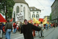 Image of sheet 20020190 photo 1: 1. Mai Demo Demonstration  gegen Busch George Bush Masken Affen Köche Koch Kochen ehemaliger Tessiner Nationalrat der Sozialdemokraten Franco Cavalli an der Demo am Limmatquai füttert Frau Tauben. 
Gotthard Wilhem Tell Abbildung auf Smart Auto Autobahn Galerien im Regen