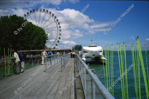 Image of sheet 20020210 photo 26: Ausflug Expo.02 mit Redaktion der Schweizer Familie Tamedia Schiff nach Neuenburg Sicht vom See Stäbe Neuchatel Die drei Kieselsteine auf der Arteplage Neuenburg 2002
Die Expo.02 war die 6. Schweizer Landesausstellung und fand vom 15. Mai bis zum 20. Oktober 2002 im Drei-Seen-Land statt. Die Ausstellung bestand hauptsächlich aus fünf Arteplage genannten Ausstellungsgeländen, welche an den Seeufern der Städte Biel/Bienne, Murten, Neuenburg und Yverdon-les-Bains ausschliesslich für die Dauer der Exposition errichtet wurden; die fünfte Arteplage war eine umgebaute Kiesbarke, Arteplage mobile du Jura genannt, die zwischen den restlichen Arteplages verkehrte. Dabei vertrat jede Arteplage einen der fünf Organisations-Kantone Bern, Jura, Freiburg, Neuenburg und Waadt.
Alis Heussler 4 1/2 jährig und Olivia Apfelsorten alte in Konfitüregläser Gläser Apfel Riesenrad Coop

Expo.02 was the 6th Swiss national exposition, which was held from 15 May to 20 October 2002. The exposition took place around the lakes of Neuchâtel, Bienne/Biel and Morat/Murten. It was divided into five sites, which were called Arteplages, due to the proximity of the water (some sites were actually partially or totally built on the water). The five Arteplages were located in Neuchâtel, Yverdon-les-Bains, Morat/Murten, Biel/Bienne and on a mobile barge traveling from one site to another. The barge represented the canton of Jura, which does not have access to any one of the three lakes. Switzerland Schweiz 2002