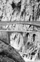 Image of sheet 20020400 photo 3: Gotthardstrasse Schöllenen Strassenbrücke von 1956 überspannt jene von 1830 die Säumerbrücke von 1200 befand sich ganz unten in der Schlucht. Viadukt Schöllenenbahn Teufelsbrücke Suwarow-Denkmal Memorial  
Urnerloch erstes Tunnel der Schweiz.
Kletterer am Klettersteig
Schülergruppe Touristen Andermatt Militärkaserne militärisches Uebungsgebiet Mic Ganz Michael
Urserental Felder Rentner Alois Regli mit Frau und Freunden vor dem 'Sybfiggler' auf Bank in Andermatt Eingang Bunker im Feld am Berg Kanton Uri, Schweiz Switzerland
Heute baut dort der ägyptische Bauunternehmer Samih Sawiri ein Ferien-resort.
aus: Gotthard, das Hindernis verbindet.