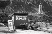 Image of sheet 20020680 photo 37: Autoschlangen auf der Nordachse des Gotthardpasses Teufelsstein am Nordportal Gotthard Strassentunnel Uri Wohnwagen Belüftungsanlage vor Operalpbahn Alis steht vor Flieger Denkmal und Passhöhentafel Gotthard Hospiz Cervelat Bratwurst Stand Urserental oberhalb Andermatt