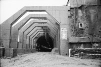 Image of sheet 20020790 photo 10: Neat Bahntunnel Gotthardbasistunnel Baustelle Suedportal
AlpTransit Gotthard AG  Südportal in Bodio 
Durchstich zur Oströhre Faido Gruppenbild Mineure zur Feier des ersten Durchbruchs im Basistunnel. 
...Wir sind zur Feier in den Gotthard-Basistunnel gekommen: den ersten Durchbruch im Jahrhundertbauwerk, nämlich von der Lockergesteinszone in die nördlich anschliessende Oströhre. Vor der Tunnelbrust steht erhöht wie auf einer Bühne ein gelber, von Scheinwerfern angestrahlter Bagger. Ende der Lockergesteinszone, die Tunnelbrust, auf der das auszubrechende Profil mit roten Punkten markiert ist, besteht aus solidem , monolithischem Leventinagranit. Die Mineure strömen in den Stollen, Lautsprecher werden montiert. ... Durch die Oeffnung sehen wir in die Oströhre hinüber...
Arbeiter der Firma Herrenknecht an der TBM
aus: Gotthard, das Hindernis verbindet. Kanton Tessin, Ticino, Schweiz Svizzera, Switzerland 2002