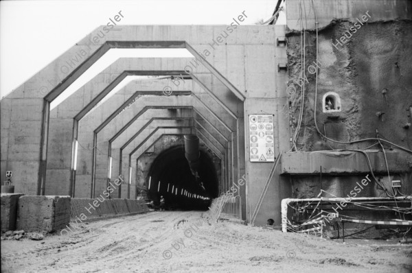 Image of sheet 20020790 photo 10: Neat Bahntunnel Gotthardbasistunnel Baustelle Suedportal
AlpTransit Gotthard AG  Südportal in Bodio 
Durchstich zur Oströhre Faido Gruppenbild Mineure zur Feier des ersten Durchbruchs im Basistunnel. 
...Wir sind zur Feier in den Gotthard-Basistunnel gekommen: den ersten Durchbruch im Jahrhundertbauwerk, nämlich von der Lockergesteinszone in die nördlich anschliessende Oströhre. Vor der Tunnelbrust steht erhöht wie auf einer Bühne ein gelber, von Scheinwerfern angestrahlter Bagger. Ende der Lockergesteinszone, die Tunnelbrust, auf der das auszubrechende Profil mit roten Punkten markiert ist, besteht aus solidem , monolithischem Leventinagranit. Die Mineure strömen in den Stollen, Lautsprecher werden montiert. ... Durch die Oeffnung sehen wir in die Oströhre hinüber...
Arbeiter der Firma Herrenknecht an der TBM
aus: Gotthard, das Hindernis verbindet. Kanton Tessin, Ticino, Schweiz Svizzera, Switzerland 2002