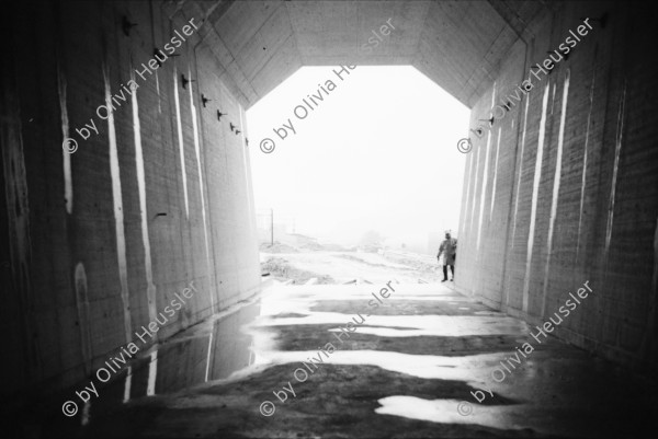 Image of sheet 20020790 photo 3: Neat Bahntunnel Gotthardbasistunnel Baustelle Suedportal
AlpTransit Gotthard AG  Südportal in Bodio 
Durchstich zur Oströhre Faido Gruppenbild Mineure zur Feier des ersten Durchbruchs im Basistunnel. 
...Wir sind zur Feier in den Gotthard-Basistunnel gekommen: den ersten Durchbruch im Jahrhundertbauwerk, nämlich von der Lockergesteinszone in die nördlich anschliessende Oströhre. Vor der Tunnelbrust steht erhöht wie auf einer Bühne ein gelber, von Scheinwerfern angestrahlter Bagger. Ende der Lockergesteinszone, die Tunnelbrust, auf der das auszubrechende Profil mit roten Punkten markiert ist, besteht aus solidem , monolithischem Leventinagranit. Die Mineure strömen in den Stollen, Lautsprecher werden montiert. ... Durch die Oeffnung sehen wir in die Oströhre hinüber...
Arbeiter der Firma Herrenknecht an der TBM
aus: Gotthard, das Hindernis verbindet. Kanton Tessin, Ticino, Schweiz Svizzera, Switzerland 2002