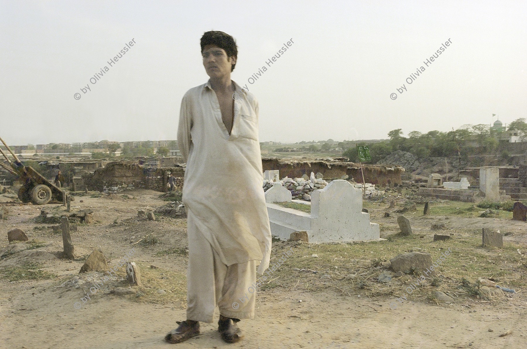 Image of sheet 20030170 photo 36: Im Flüchtlingslager des UNHCR für afghanische Flüchtlinge in Islamabad. F-11
OBJE_Pakistan: Islamabad, Slum F-11. Afghan Refugee stand in front of the graveyard.The Camp is  runned by UNHCR 26/05/2003 Pakistan: Afghanischer Flüchtling auf dem Friedhof im Flüchtlingslager