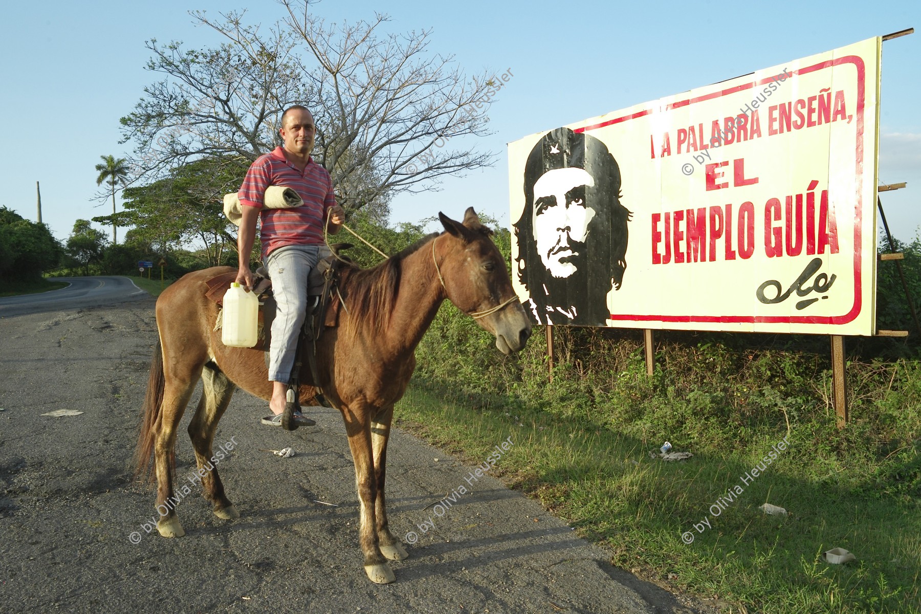 Image of sheet 20140210 photo 46: Ein Mann auf einem Pferd steht vor einer Propaganda Tafel 
«La palabra enseña, el ejemplo guia» Che Das Wort lehrt, das Beispiel führt. Steht mit dem Abbild Che Guevaras an einer Strasse Richtung Viñales Kuba 2014 Cuba Werbung politische Publicity