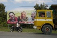 Image of sheet 20140214 photo 75: Lastwagen und Motorrad vor einem Plakat mit v.l.n.r. Hugo Chavez, Fidel Castro und Nelson Mandela, Cuba 2014.